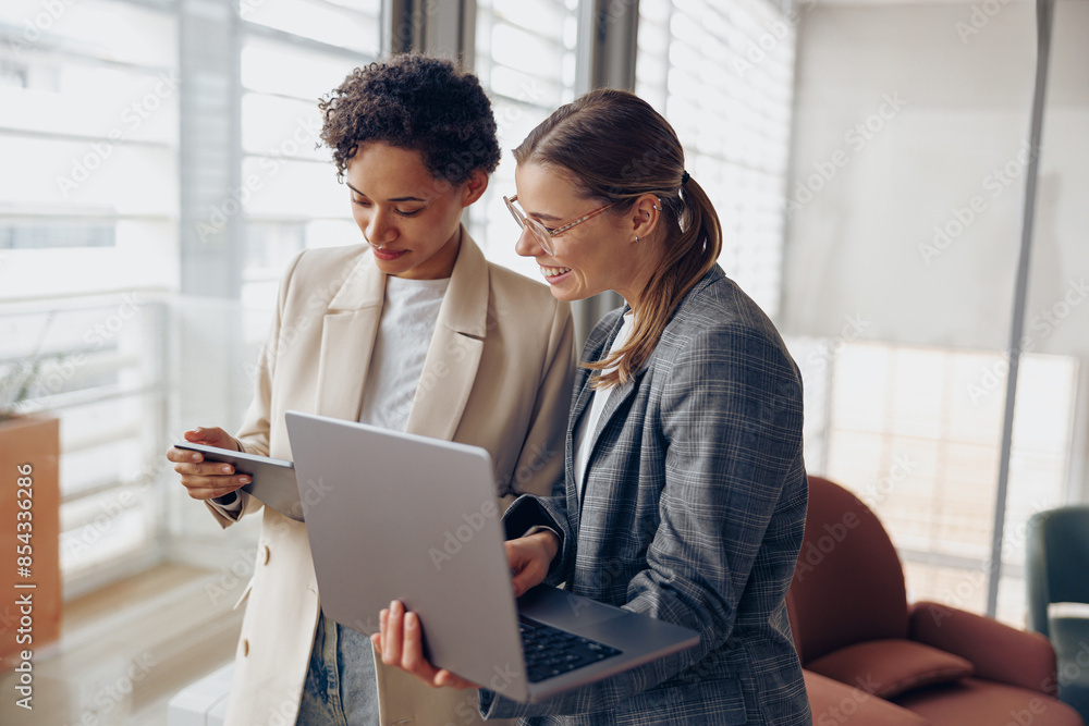 Group of female managers standing in modern office while working on laptop and digital tablet Group of female managers standing in modern office while working on laptop and digital tablet