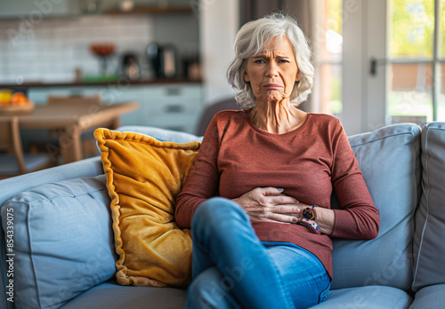 Mid-aged woman with stomach pain sitting sadly on couch