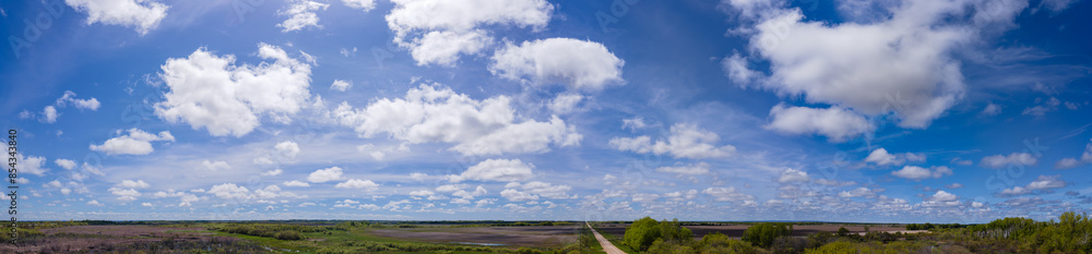 A wide drone aerial panoramic view of a blue sky with white clouds above a prairie agricultural landscape, a road runs through the center of the frame and disappears into the distance.
A wide drone aerial panoramic view of a blue sky with white clouds above a prairie agricultural landscape, a road runs through the center of the frame and disappears into the distance.