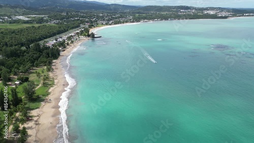 aerial footage of luquillo beach with palm trees and waves crashing tropical island getaway in puerto rico view of el yunque rainforest mountains hills background boat on sea water ocean caribbean photo