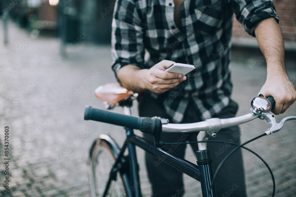 Obraz premium Man using smartphone while riding bicycle in city