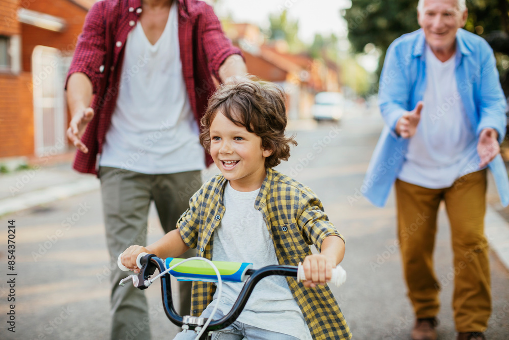 Obraz premium Father and grandfather teaching young boy to ride a bike on residential street