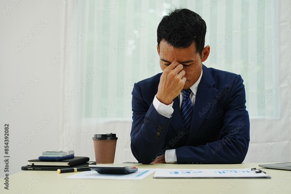 stressed businessman is sitting at his office desk, looking worried while working on his laptop. Overworked and frustrated, he faces financial problems and job pressures in his corporate banking role stressed businessman is sitting at his office desk, looking worried while working on his laptop. Overworked and frustrated, he faces financial problems and job pressures in his corporate banking role