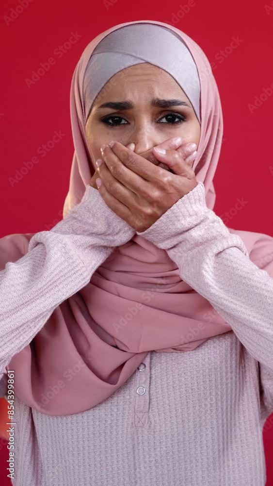 Vertical video. Fear stress. Anxiety attack. Oops embarrassment. Disturbed scared woman in headscarf covering mouth with hands isolated on red. Vertical video. Fear stress. Anxiety attack. Oops embarrassment. Disturbed scared woman in headscarf covering mouth with hands isolated on red.