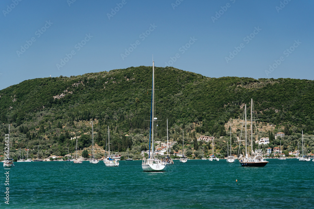 Yachts and sailboats moored in a serene bay, with a green hill in the background under a clear blue sky, depicting a peaceful maritime scene. Yachts and sailboats moored in a serene bay, with a green hill in the background under a clear blue sky, depicting a peaceful maritime scene.