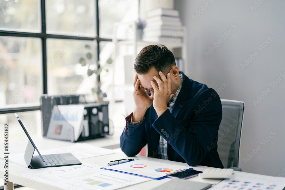 Businessman Stressed at Work Desk with Laptop and Documents in Modern Office Businessman Stressed at Work Desk with Laptop and Documents in Modern Office