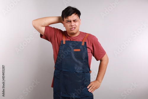 Young handsome asian man wearing apron standing over white background confuse and wonder about question. Uncertain with doubt, thinking with hand on head. Pensive concept. photo