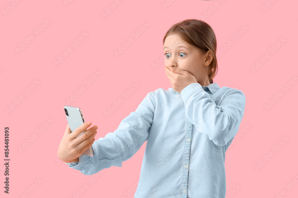 Shocked little girl with mobile phone on pink background