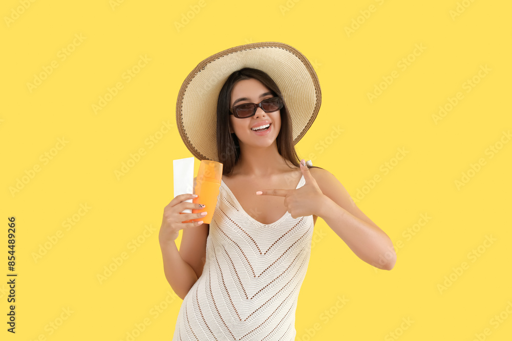 Beautiful young woman pointing at sunscreen cream on yellow background Beautiful young woman pointing at sunscreen cream on yellow background