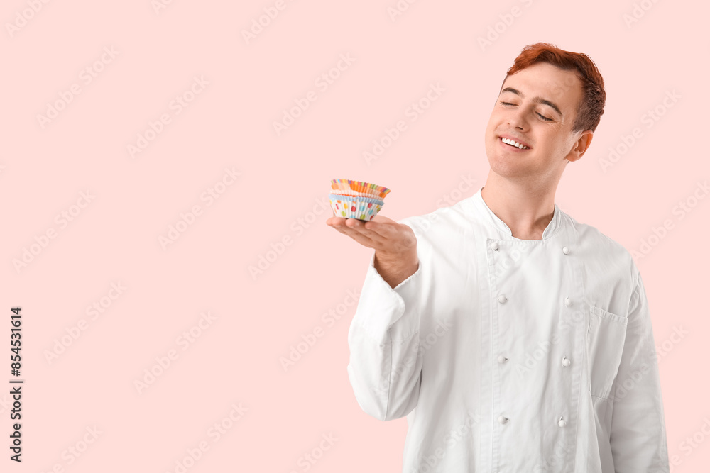 Male confectioner in uniform with cupcake molds on pink background Male confectioner in uniform with cupcake molds on pink background