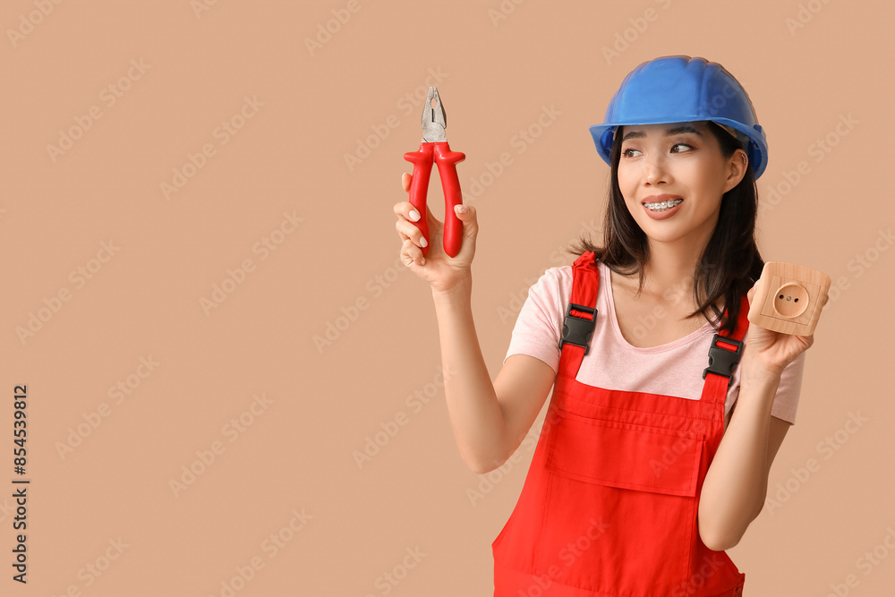 Young female electrician with pliers and socket on beige background Young female electrician with pliers and socket on beige background