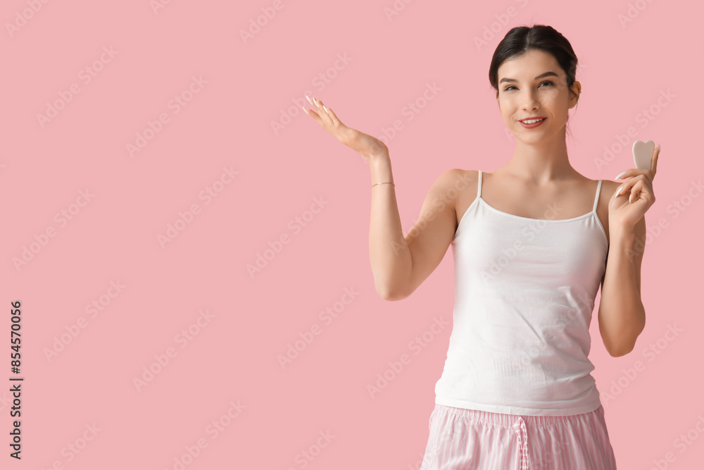 Beautiful young happy woman with guasha tool pointing at something on pink background Beautiful young happy woman with guasha tool pointing at something on pink background