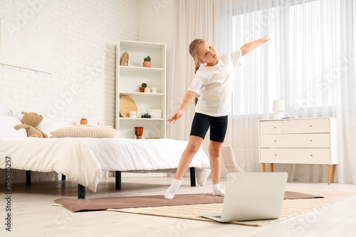 Cute little girl with mat and laptop practicing in gymnastics bedroom