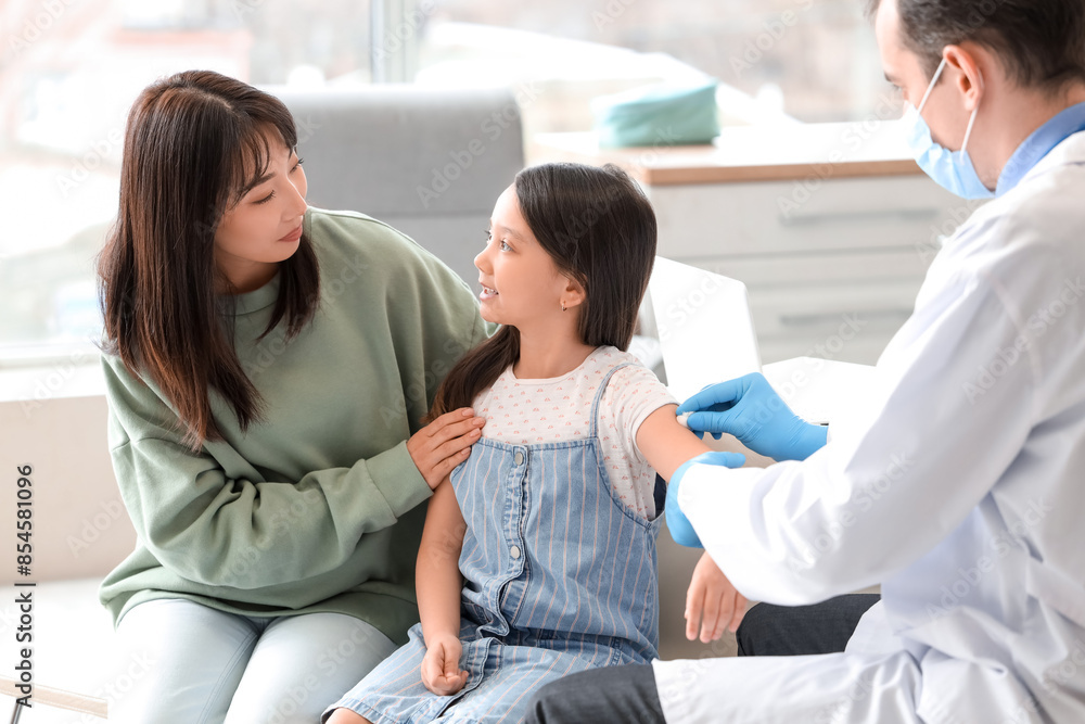 Fototapeta premium Little Asian girl with her mother receiving vaccine in clinic
