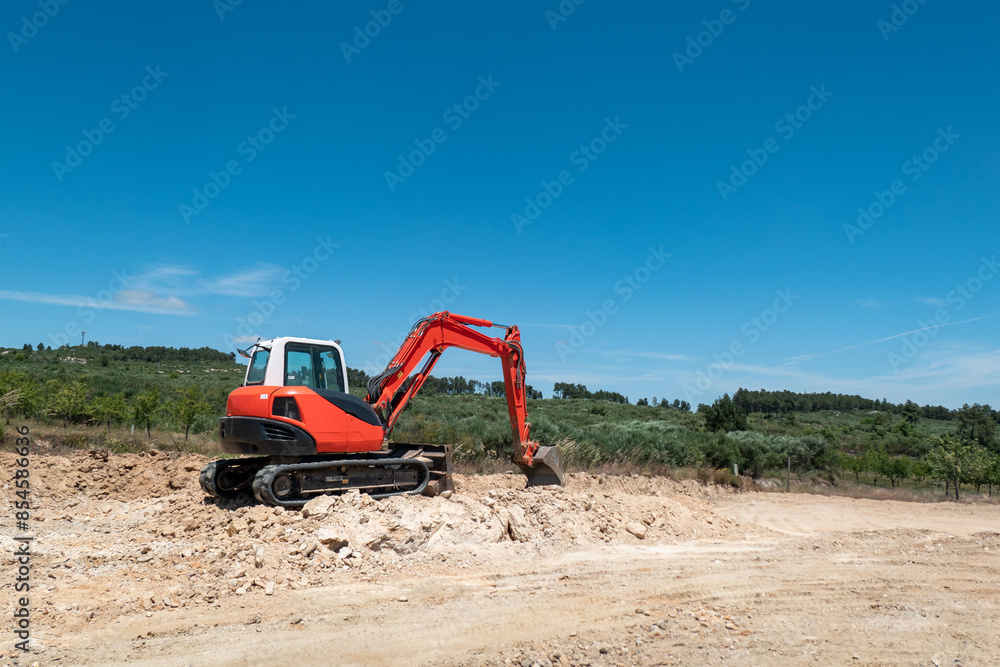 Retroescavadora de esteiras a operar num terreno rochoso para a construção de uma estrada sob um céu azul e em meio à natureza Retroescavadora de esteiras a operar num terreno rochoso para a construção de uma estrada sob um céu azul e em meio à natureza