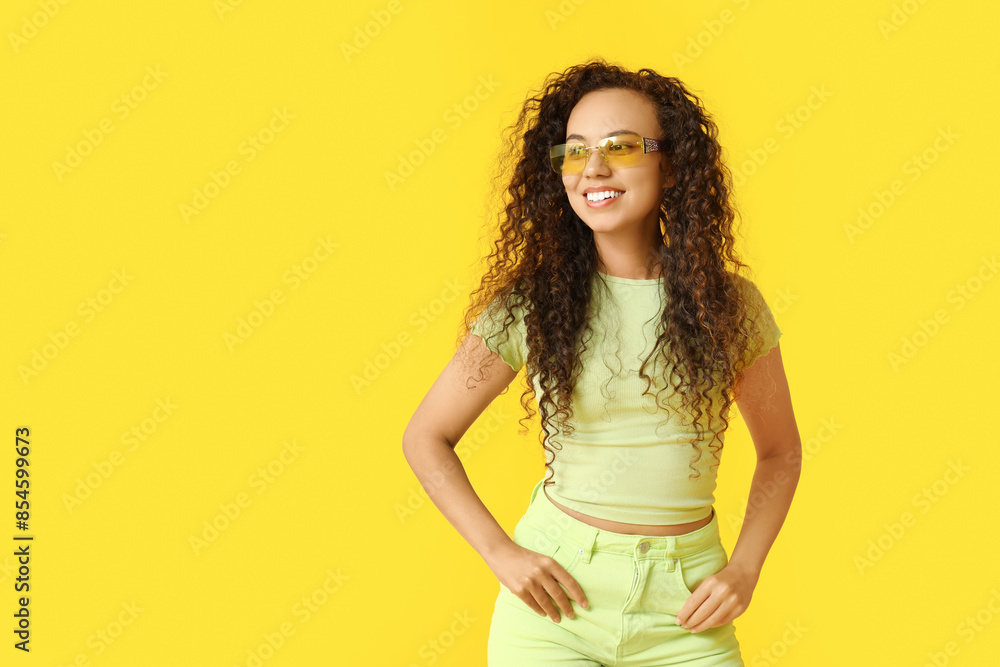 © Pixel-Shot - Happy young African-American woman in sunglasses on yellow background