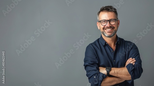 Obraz na płótnie Smiling bearded man with glasses in casual wear standing with his arms crossed against gray background. Professional and friendly vibe for corporate or business use. This is a concept image. AI w salonie