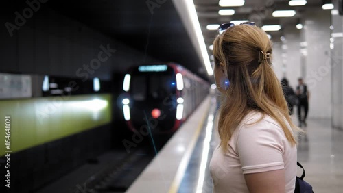 Side view of a young woman with a backpack at the metro station, the train is moving along the rails. A woman in the subway is waiting for a train. photo