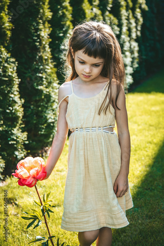 A little girl in yellow dress in the garden, holding a big pink peony flower