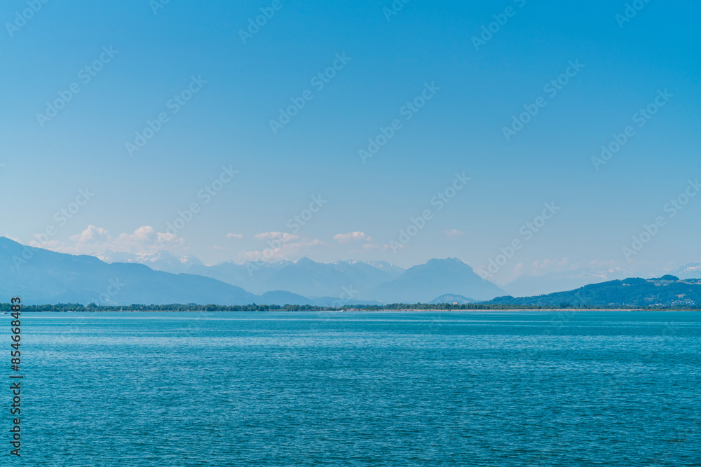 Germany, enchanting view to white snow covered mountain peaks of alps from lindau in summer with blue sky panorama behind water of bodensee lake