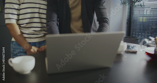 Asian couple standing close to each other. Launching computer. Opening lid of laptop. Waving their hands to camera. Remote communication with friends or relatives. Relaxing in kitchen. photo