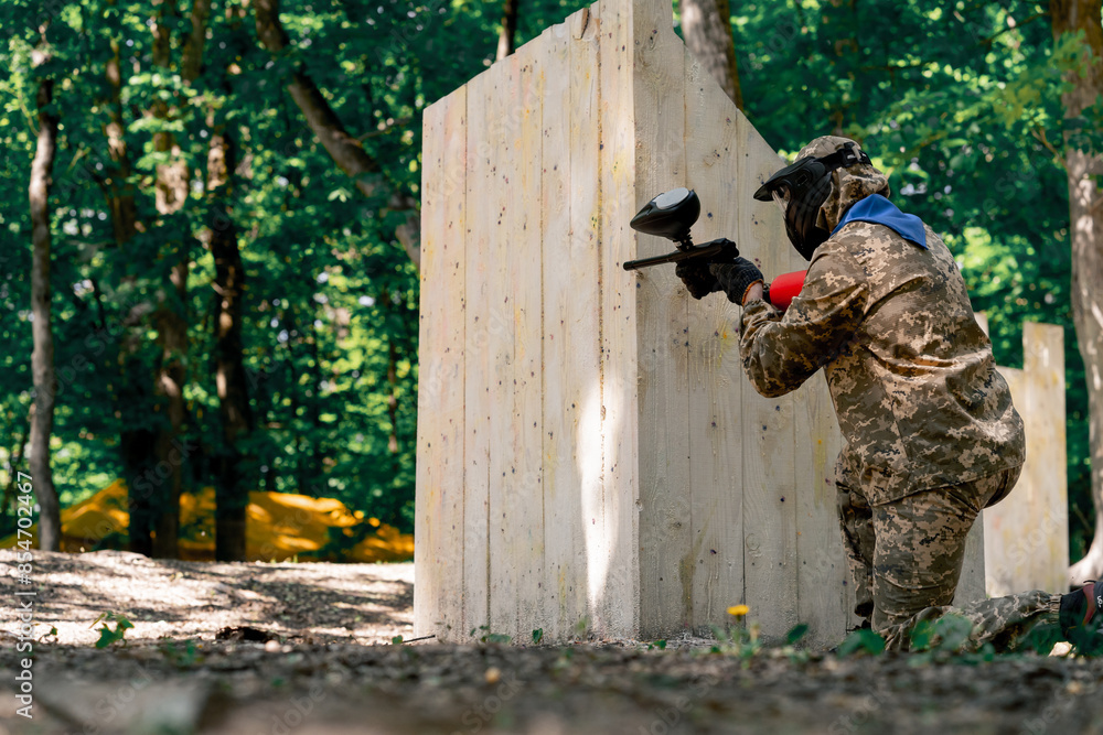 Fototapeta premium in the wild near tree structures player in a pintball uniform holds a pistol with a red balloon team game camouflage clothing
