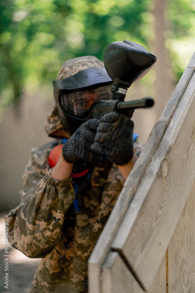 Fototapeta premium close up in the wild near tree structures player in a pintball uniform holds a pistol with a red balloon team game camouflage clothing