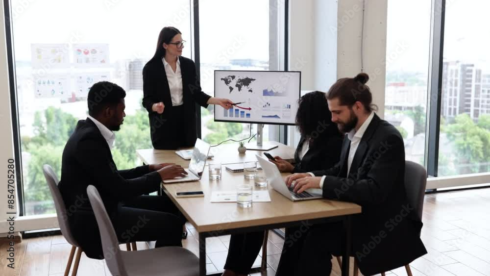 Caucasian business woman makes a report to multiracial, multinational, multicultural colleagues standing near monitor with graphs, charts. Diverse business people sit at table and clap their hands. Caucasian business woman makes a report to multiracial, multinational, multicultural colleagues standing near monitor with graphs, charts. Diverse business people sit at table and clap their hands.