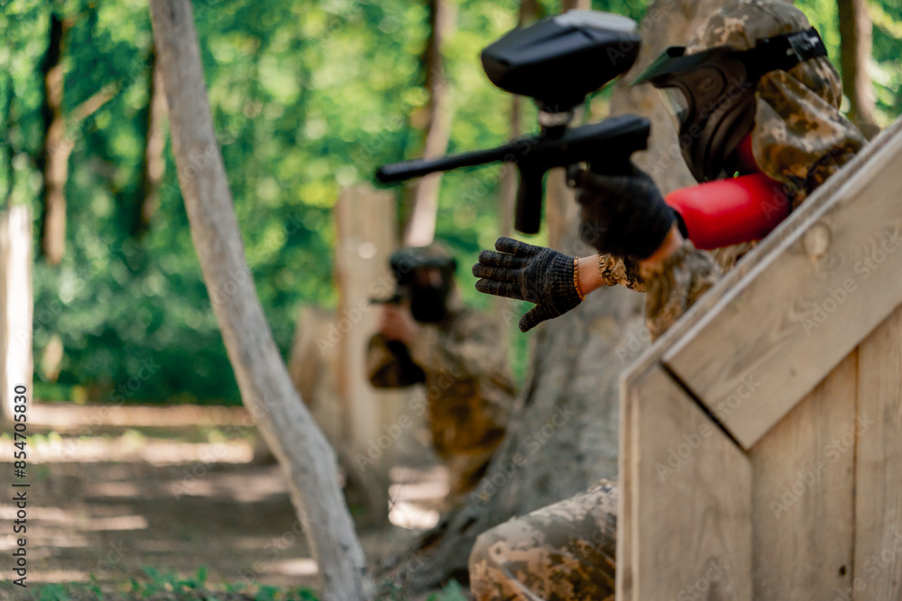 Obraz premium in the wild near tree structures player in a pintball uniform holds a pistol with a balloon team game camouflage clothing communication using hands