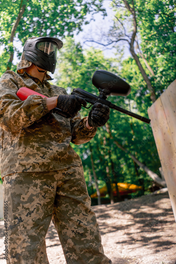 Naklejka premium in the wild near tree structures player in a pintball uniform holds a pistol with a red balloon team game camouflage clothing