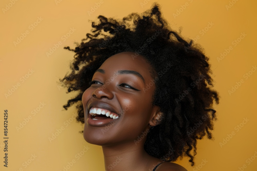 Portrait of a tender afro-american woman in her 20s laughing while standing against soft yellow background Portrait of a tender afro-american woman in her 20s laughing while standing against soft yellow background