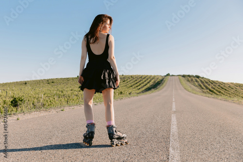 Brunette young woman roller skating outdoors on sunny day