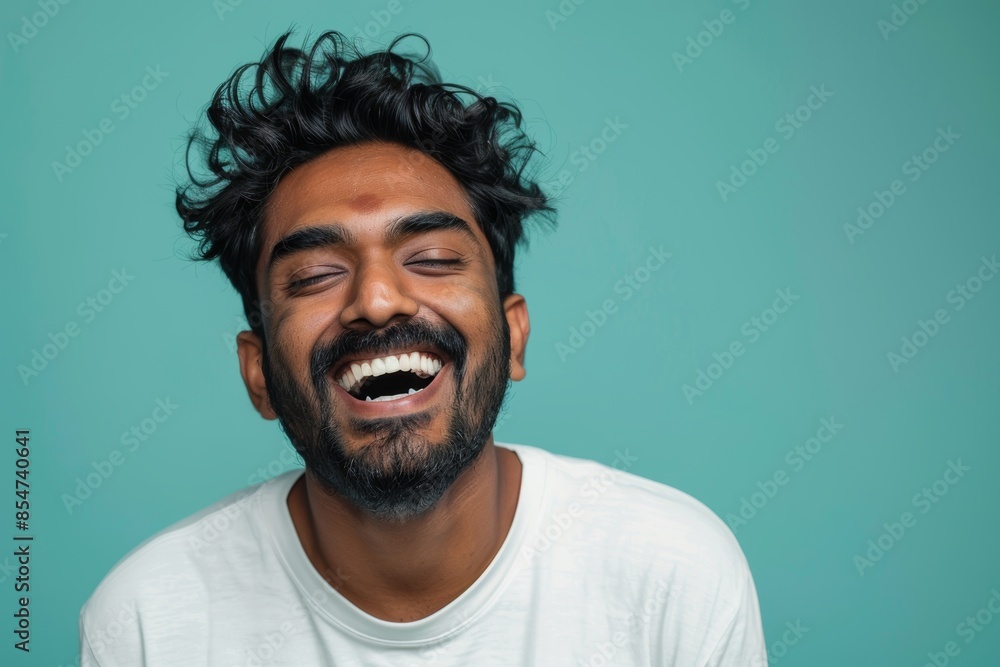 Portrait of a content indian man in his 30s laughing over soft teal background Portrait of a content indian man in his 30s laughing over soft teal background