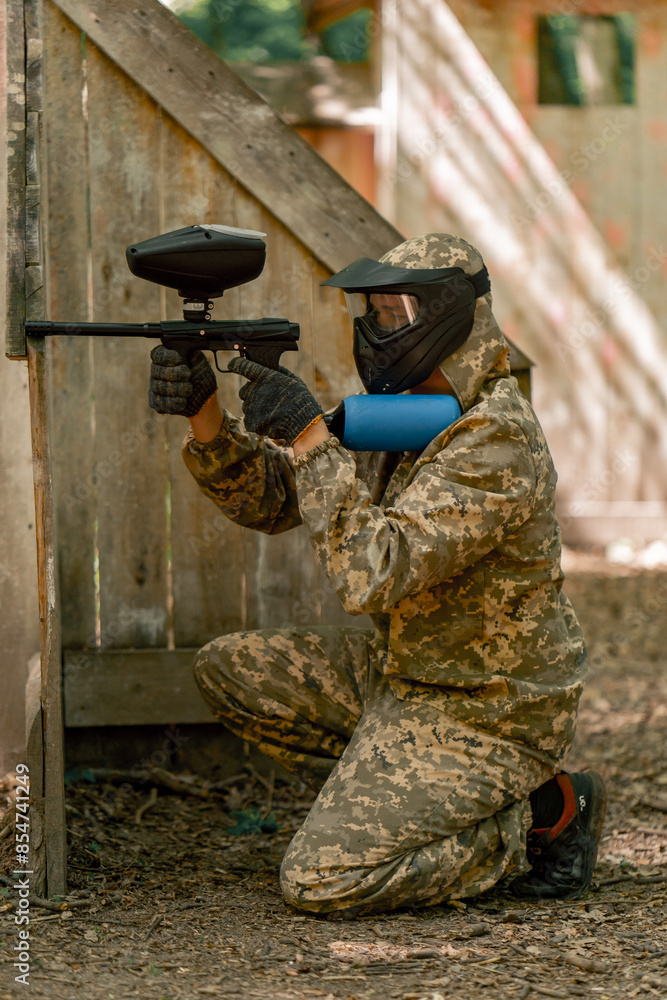 Obraz premium in the wild near tree structures player in a pintball uniform holds a pistol with a blue balloon team game camouflage clothing