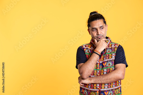 Pensive Indian man deep in thoughts, doing ruminating hand gesturing, isolated over studio background. Unsure person doing stroking chin gesture, thinking, studio backdrop
