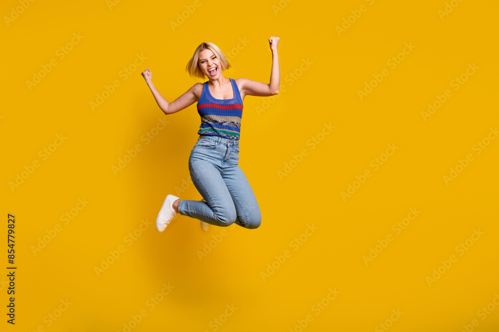 Full body length photo of sporty funny jumping woman in jeans and singlet raised fists up winning free travel tickets isolated on yellow color background Full body length photo of sporty funny jumping woman in jeans and singlet raised fists up winning free travel tickets isolated on yellow color background