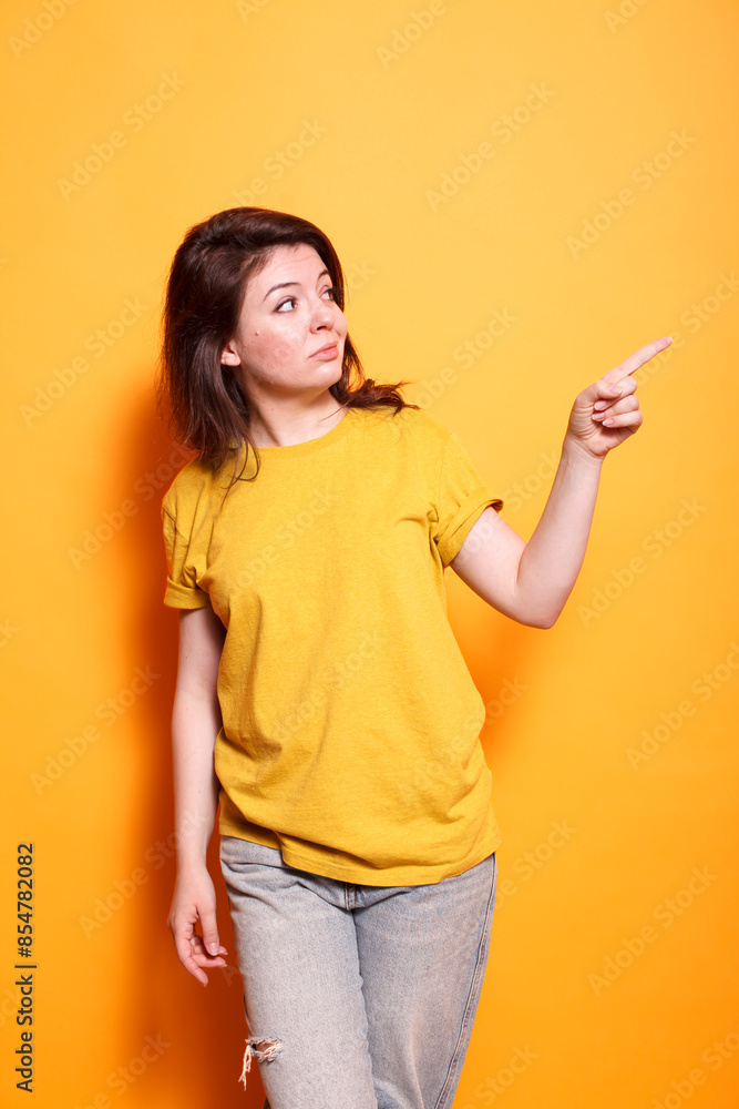 Casually dressed caucasian lady standing in front of isolated background motioning to her left side. Portrait of woman pointing and motioning with her index finger. Advertising concept. Casually dressed caucasian lady standing in front of isolated background motioning to her left side. Portrait of woman pointing and motioning with her index finger. Advertising concept.