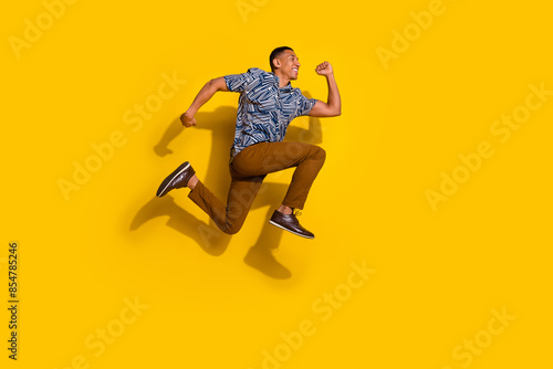 Full length photo of attractive funny guy wear print shirt jumping high running emtpy space isolated yellow color background photo