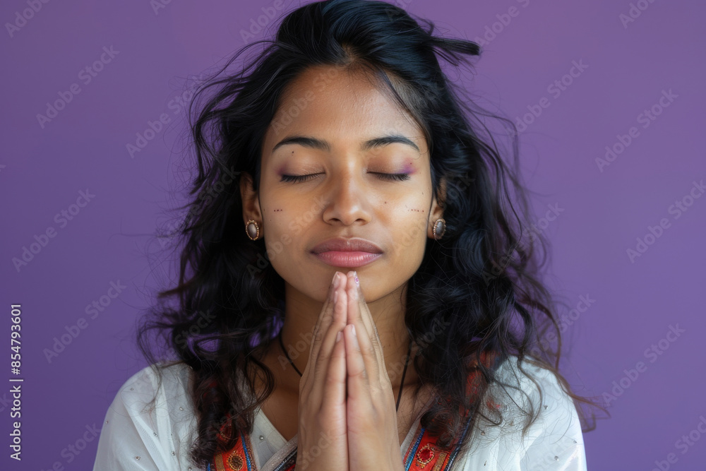 an Indian woman praying with her eyes closed: She stands with her hands folded and eyes closed, a peaceful expression on her face on a purple studio background an Indian woman praying with her eyes closed: She stands with her hands folded and eyes closed, a peaceful expression on her face on a purple studio background