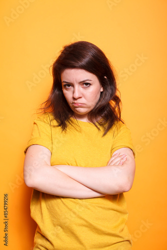 Woman standing in studio with crossed arms, disapproving and displeased facial expression on camera. Portrait of a dissatisfied person striking a grumpy and solemn expression.