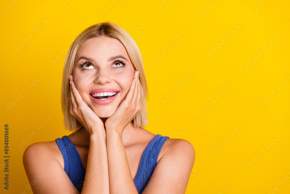 Photo portrait of young sweet beautiful woman student in singlet touching cheeks surprised looking above isolated on yellow color background Photo portrait of young sweet beautiful woman student in singlet touching cheeks surprised looking above isolated on yellow color background
