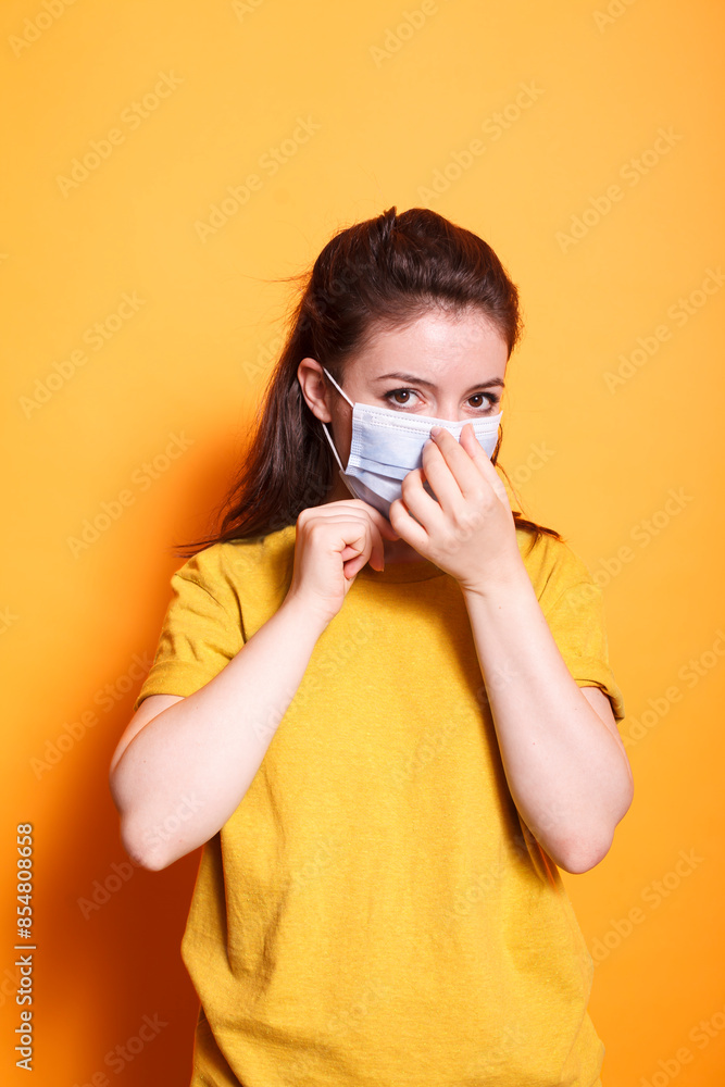 Image shows young lady adjusting a protective mask over her mouth for safety against coronavirus. Portrait of caucasian woman wearing a face mask for protection.