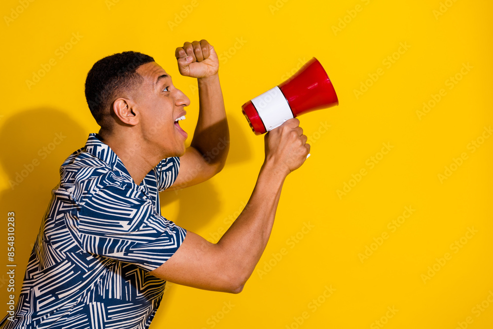 Photo of handsome lucky guy wear print shirt screaming loud speaker emtpy space isolated yellow color background Photo of handsome lucky guy wear print shirt screaming loud speaker emtpy space isolated yellow color background
