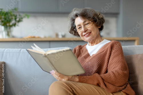 Aged woman sitting on couch and reading book pastime daydream, senior lady enjoying free time at home photo