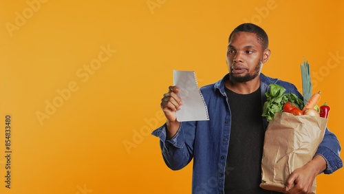 Fotografie Vegan person checking his grocery shopping list to buy everything he needs for a healthy nutrition, seeing that he forgot an important ingredient from the local zero waste store