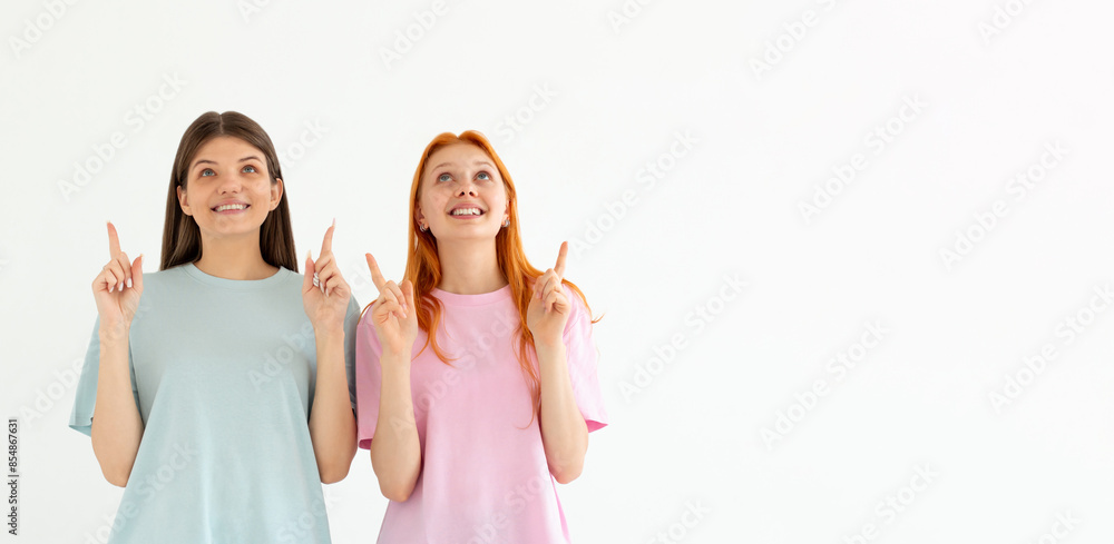 Naklejka premium Happy beautiful girls point up isolated on white background, two girls showing something above their heads , advertisement, place for text, body language