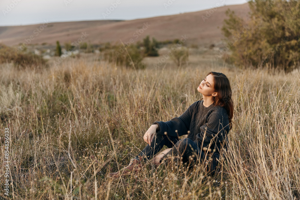 Tranquil woman sitting peacefully in tall grass with eyes closed in the middle of field Tranquil woman sitting peacefully in tall grass with eyes closed in the middle of field