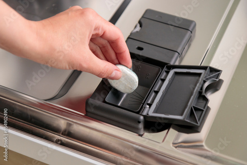 Dishwasher tablets, woman puts the capsule in the dishwashing machine before washing tableware and cutlery. Cropped view