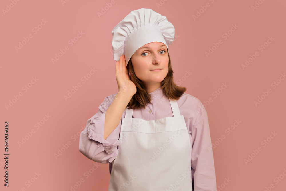 Woman chef put her hand to her ear on a studio pink background. Portrait of a female person in chef's clothing Woman chef put her hand to her ear on a studio pink background. Portrait of a female person in chef's clothing