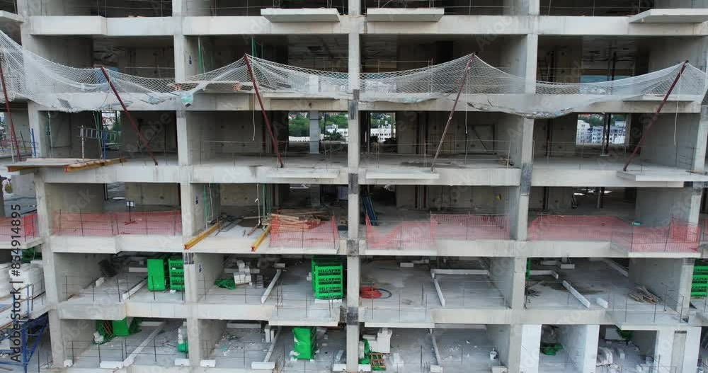 Aerial view of a large urban building construction site. Complex structure of a large building construction site, showcasing multiple floors with safety nets and construction materials. Aerial view of a large urban building construction site. Complex structure of a large building construction site, showcasing multiple floors with safety nets and construction materials.